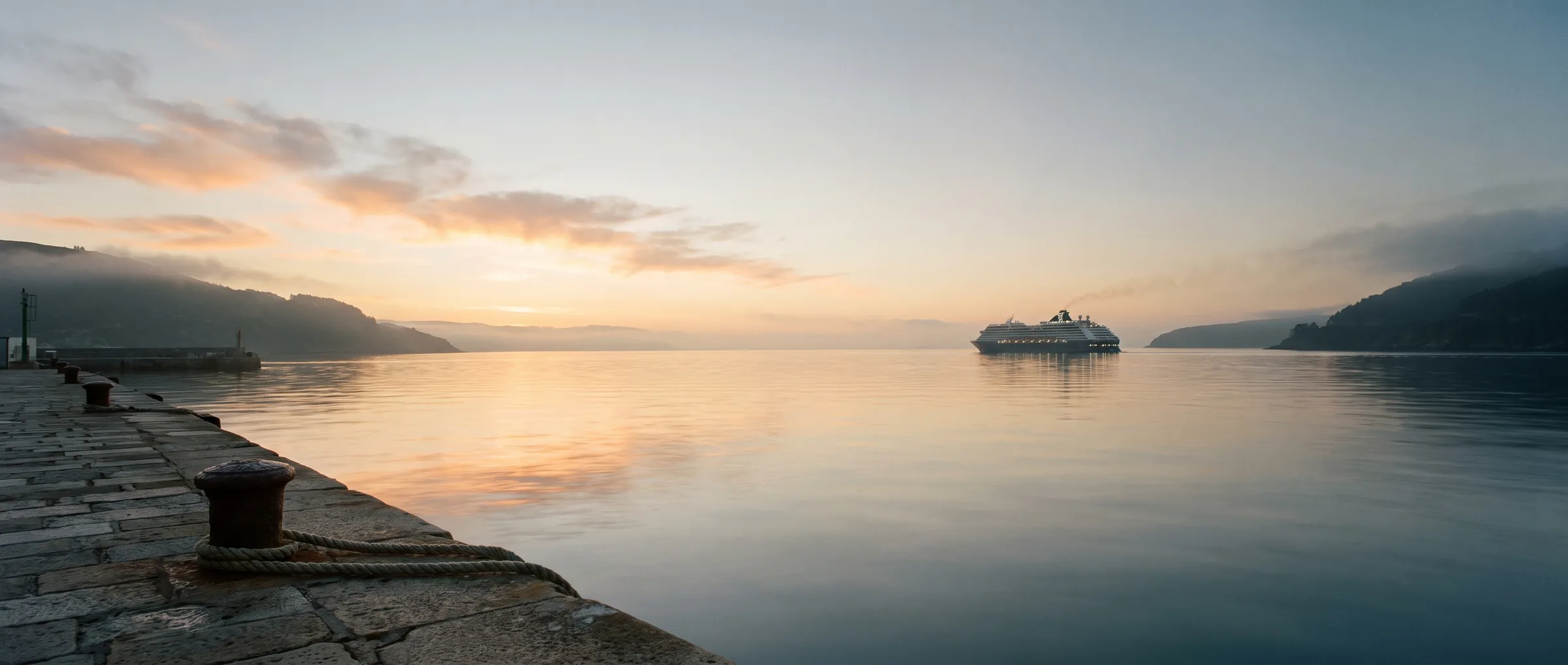 A cruise ship leaving a Northern European harbour at first light, seen from a quiet stone pier